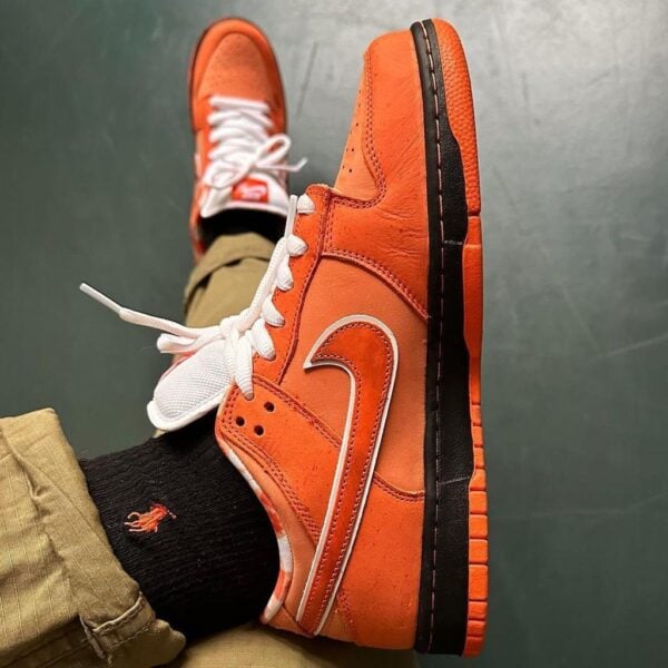 Orange high-top sneakers with white laces and black sole, worn with khaki pants and black socks.
