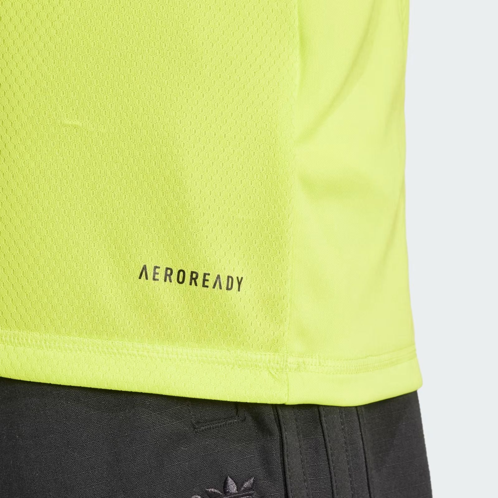 fFAWf6JusKmHbZW | UAE SPORT STORE Close-up of neon yellow athletic jersey fabric with the 'AEROREADY' logo near the hem and dark shorts below.