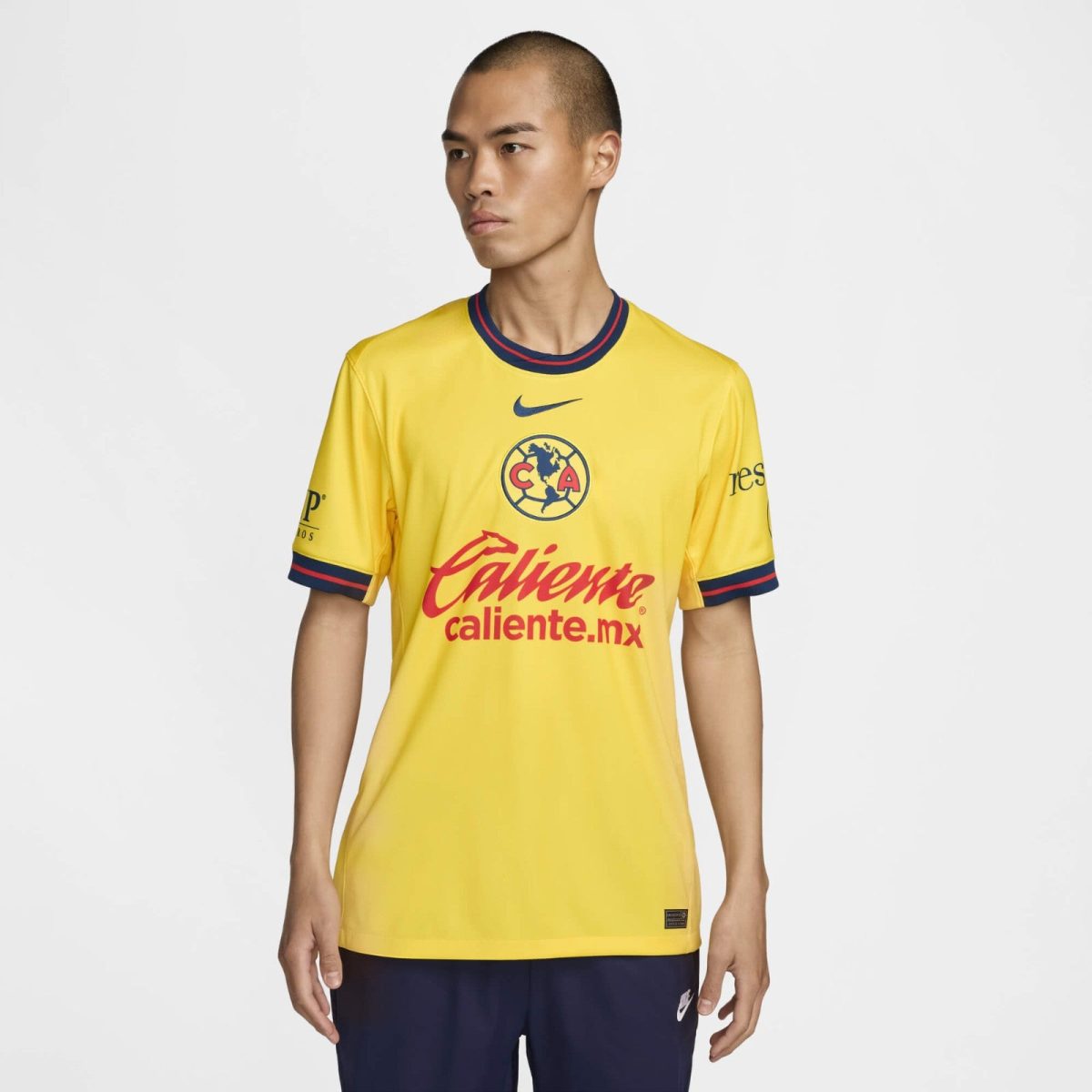 Person wearing a yellow soccer jersey with blue-red trim, featuring a crest and the red 'Caliente' sponsor front and center.