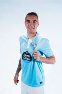 Smiling man in a light blue team jersey with sponsor logo, fist extended toward the camera.
