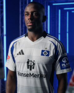 Portrait of a Black male footballer in a white Hamburger SV jersey with blue stripes, standing in a blue neon-lit studio.