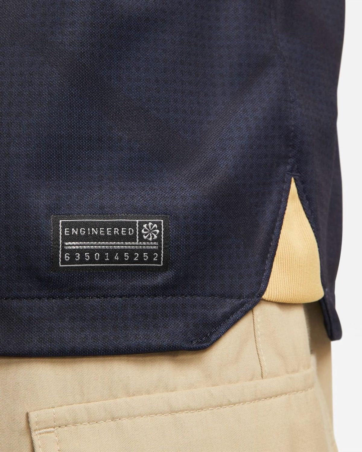 Close-up of navy fabric with a rectangular Engineered label and serial numbers stitched near the hem.