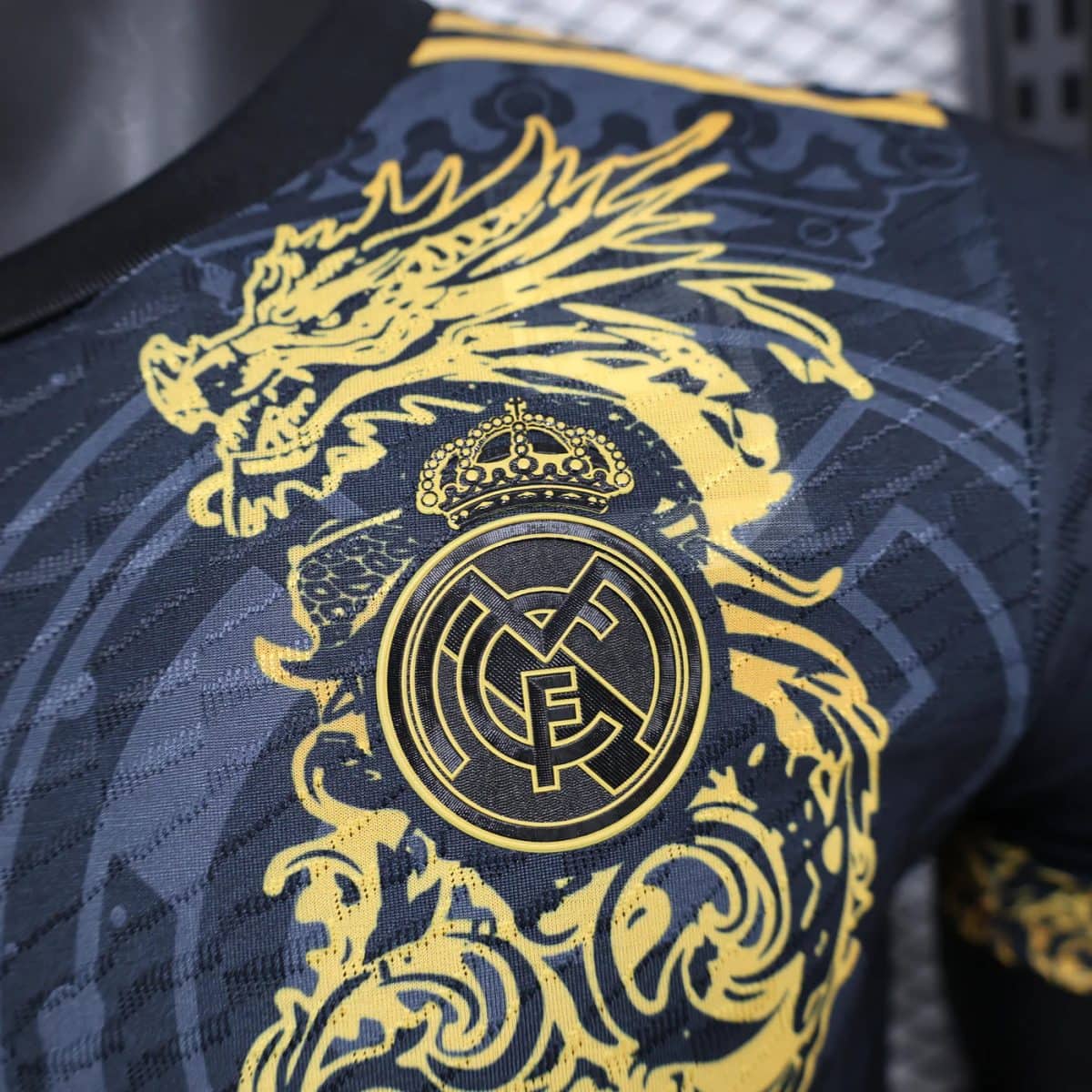 Close-up of a gold Real Madrid crest with crown on a dark patterned fabric (jersey).