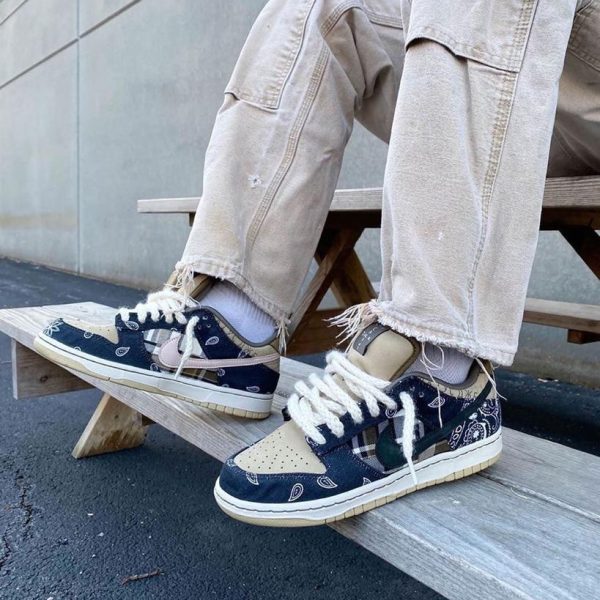 Beige cargo pants with frayed hems worn over navy and beige sneakers with white laces on a wooden bench outdoors.