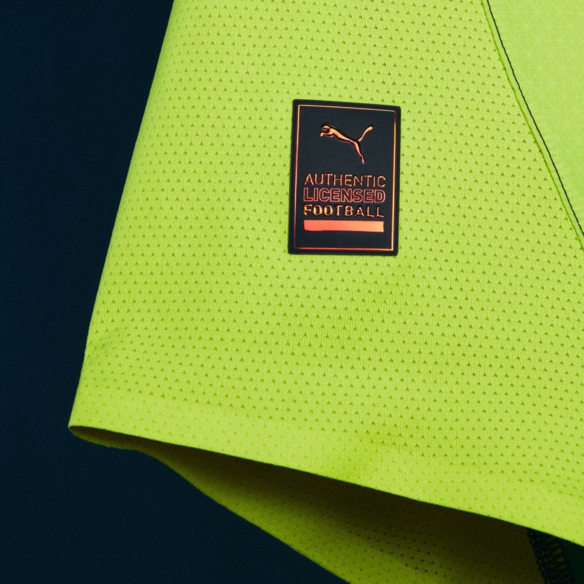 Close-up of bright neon athletic fabric with a black label reading 'Authentic Licensed Football' and a leaping Puma logo.