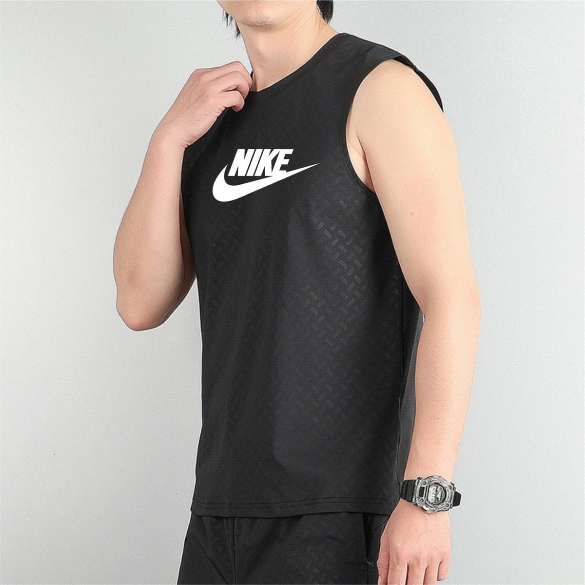 Person wearing a black sleeveless Nike athletic top, touching the collar with a watch on the left wrist