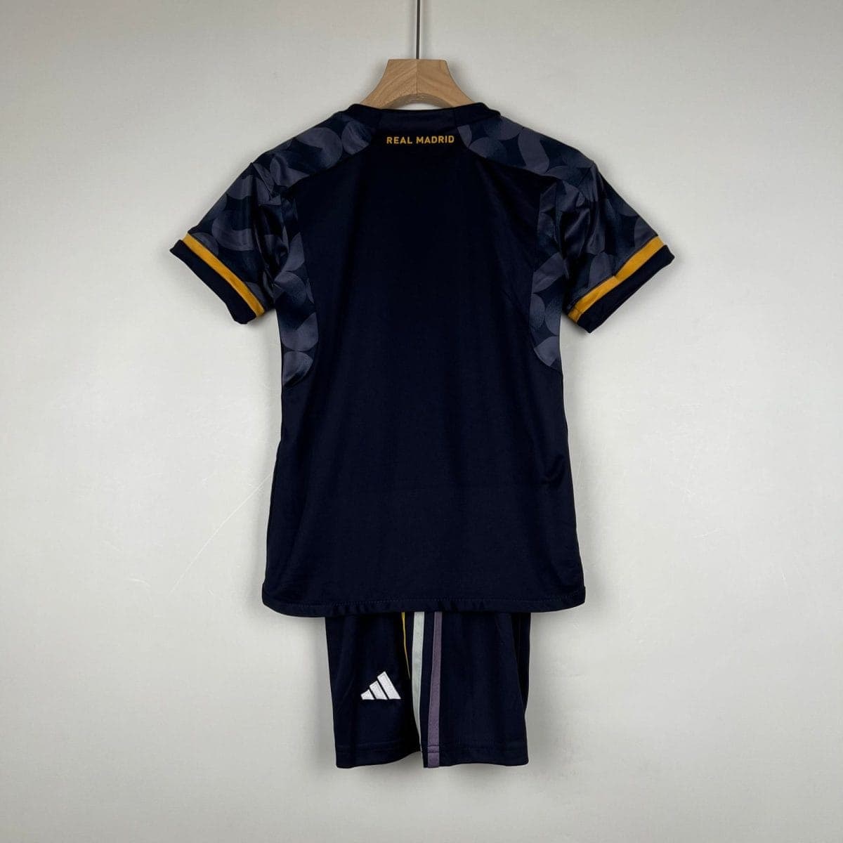 Rear view of a navy Real Madrid football jersey on a wooden hanger; camo-pattern sleeves with yellow cuffs visible at the edges.