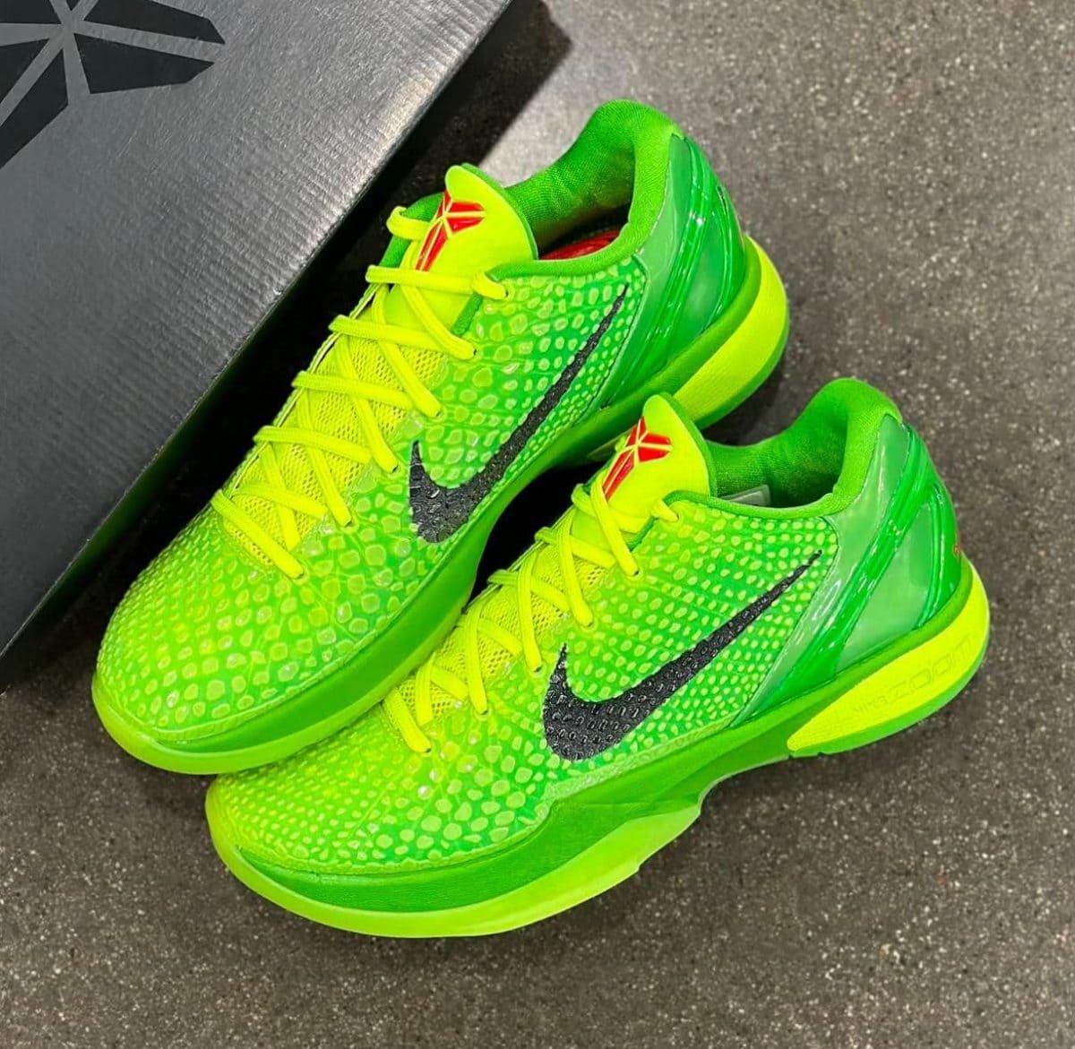 Bright neon-green running shoes with yellow laces and a black Nike swoosh, resting near a dark box on a gray floor.