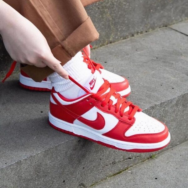 Person tying red and white Nike sneakers on concrete steps, mid-lace.