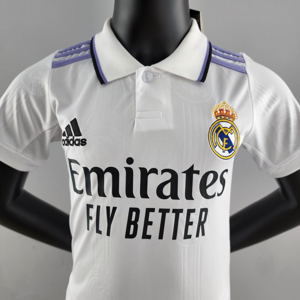 Close-up of a white Real Madrid jersey on a black mannequin, showing the Adidas logo and Real Madrid crest on the chest area.