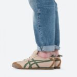 Side view of a person wearing rolled-up light-wash jeans and beige sneakers with green and brown stripes on a white background