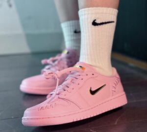 Pair of pink Nike sneakers with black swoosh on a dark floor, white crew socks showing above the shoes.