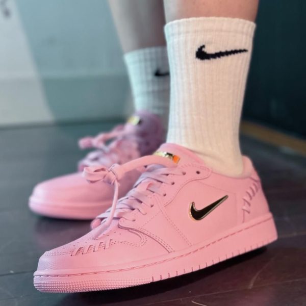 Pair of pink Nike sneakers with black swoosh on a dark floor, white crew socks showing above the shoes.