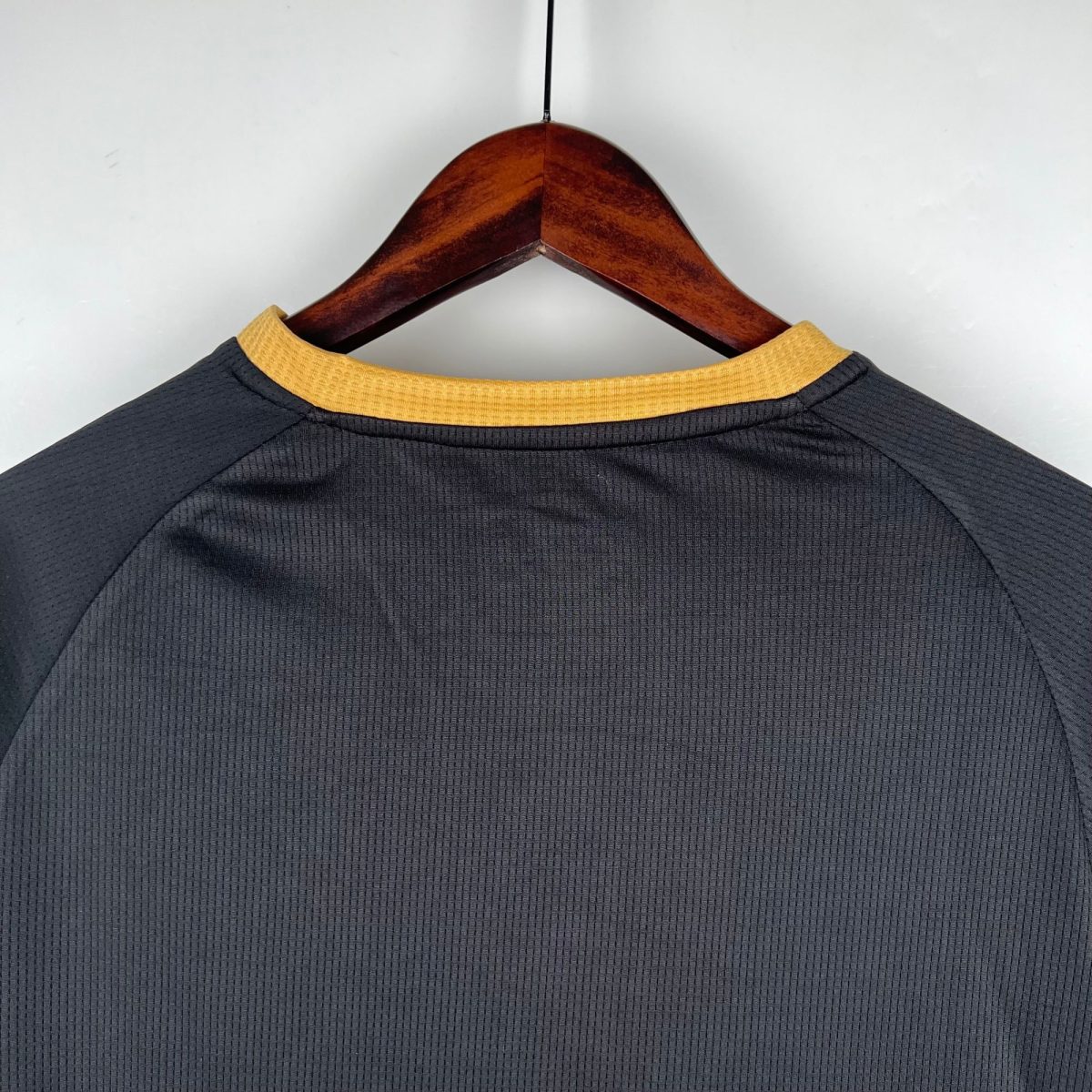Wooden hanger with a dark textured shirt featuring a yellow collar, photographed from behind against a light background.