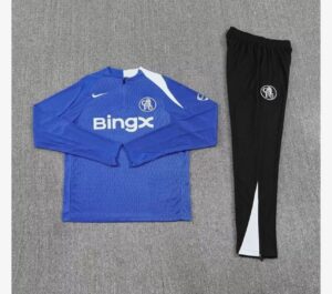 Chelsea FC blue training jersey with BingX sponsor and white accents, paired with black club-crest track pants on a gray surface