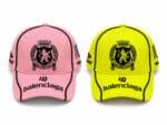 Two Balenciaga baseball caps, pink and neon yellow, each with a black crest emblem and brand text on the front and bill at the brim.
