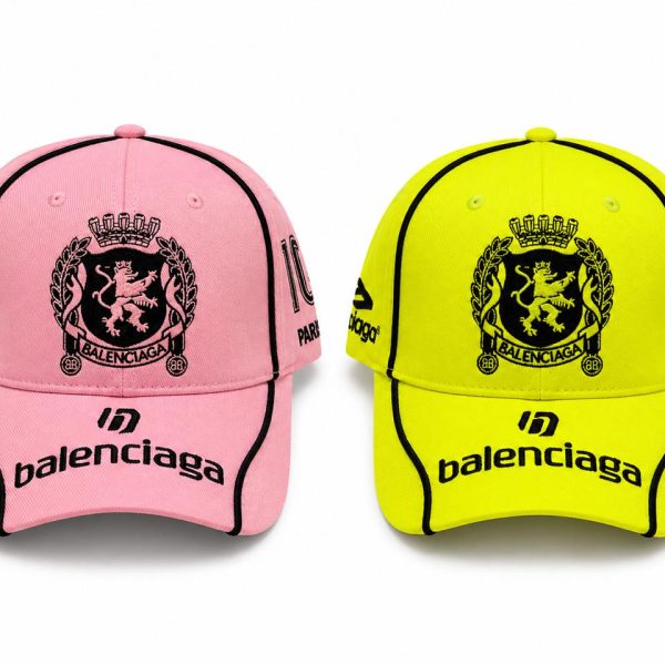 Two Balenciaga baseball caps in pink and neon yellow with black crest and ‘balenciaga’ branding visible on the bill and sides.