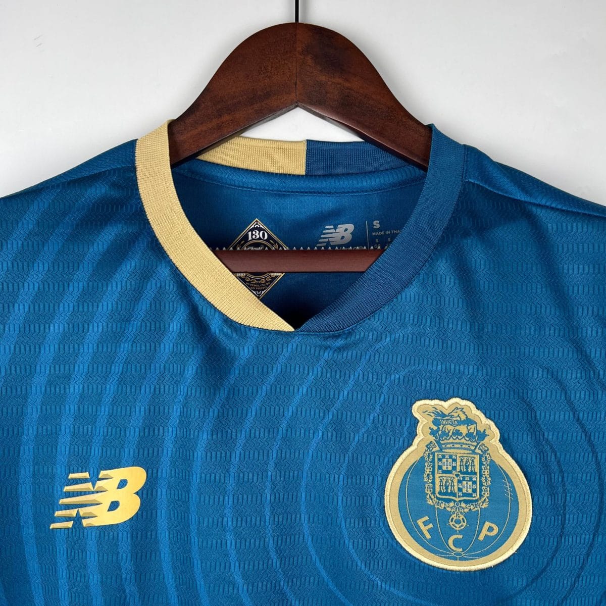 Blue athletic jersey hanging on a wooden hanger with a beige strap crossing the chest area and a crest badge near the bottom right of the image.