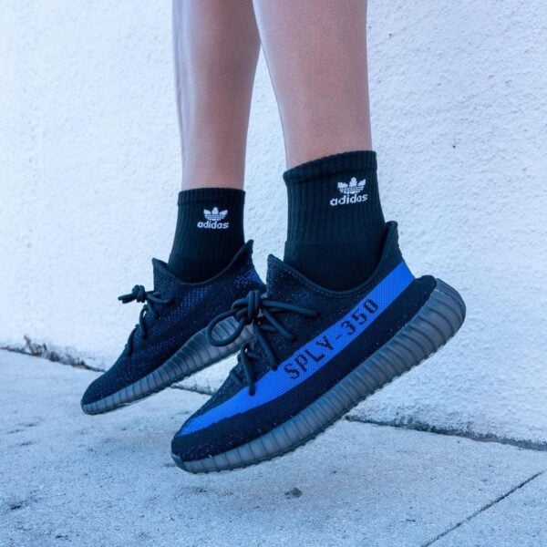 Person wearing black Adidas sneakers with blue SPLY-350 stripe and black socks standing on a concrete surface.