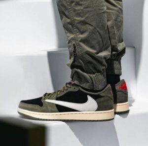 Olive and black Nike sneakers with a white swoosh worn by a person standing on white steps, beige sole visible.