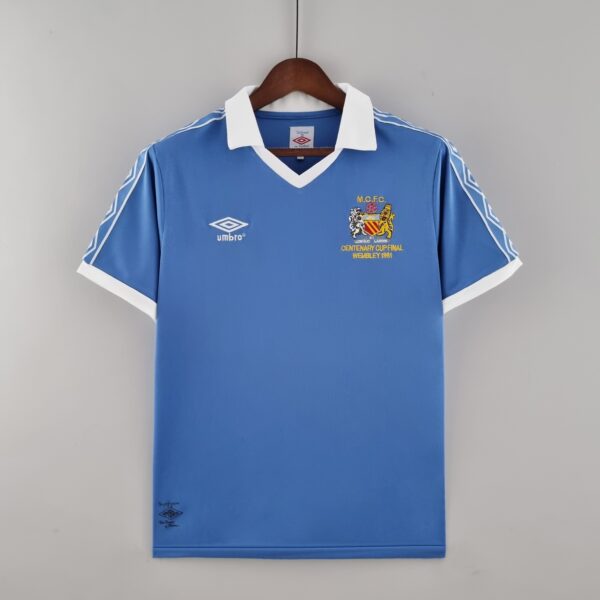 Blue Manchester City football shirt on a wooden hanger, white collar and cuffs, with Umbro branding and a crest reading 'MCFC Centenary Cup Final Wembley 1981' on the chest.