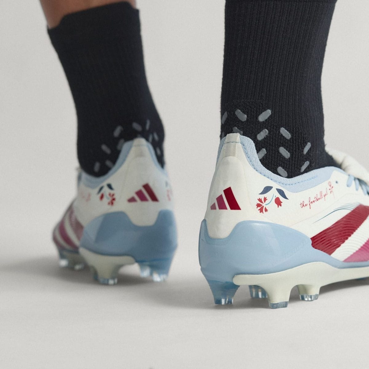 Close-up of two blue-and-white soccer cleats on black socks with studs visible on the soles, against a light background.