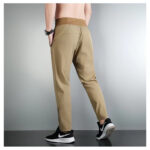 Back view of a person wearing beige athletic jogger pants and black sneakers with white soles.