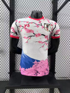 White athletic jersey with pink cherry blossoms and red accents on the collar and sleeves, featuring a Japan crest on the chest and a Y-3 logo nearby, displayed on a mannequin.
