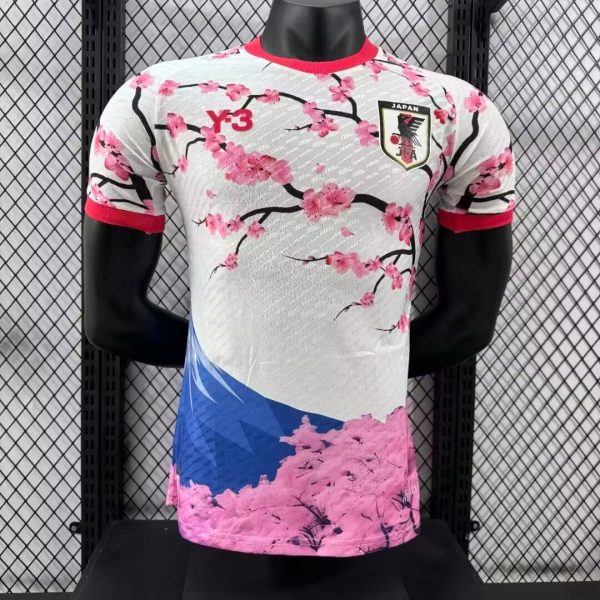 White athletic jersey with pink cherry blossoms and red accents on the collar and sleeves, featuring a Japan crest on the chest and a Y-3 logo nearby, displayed on a mannequin.