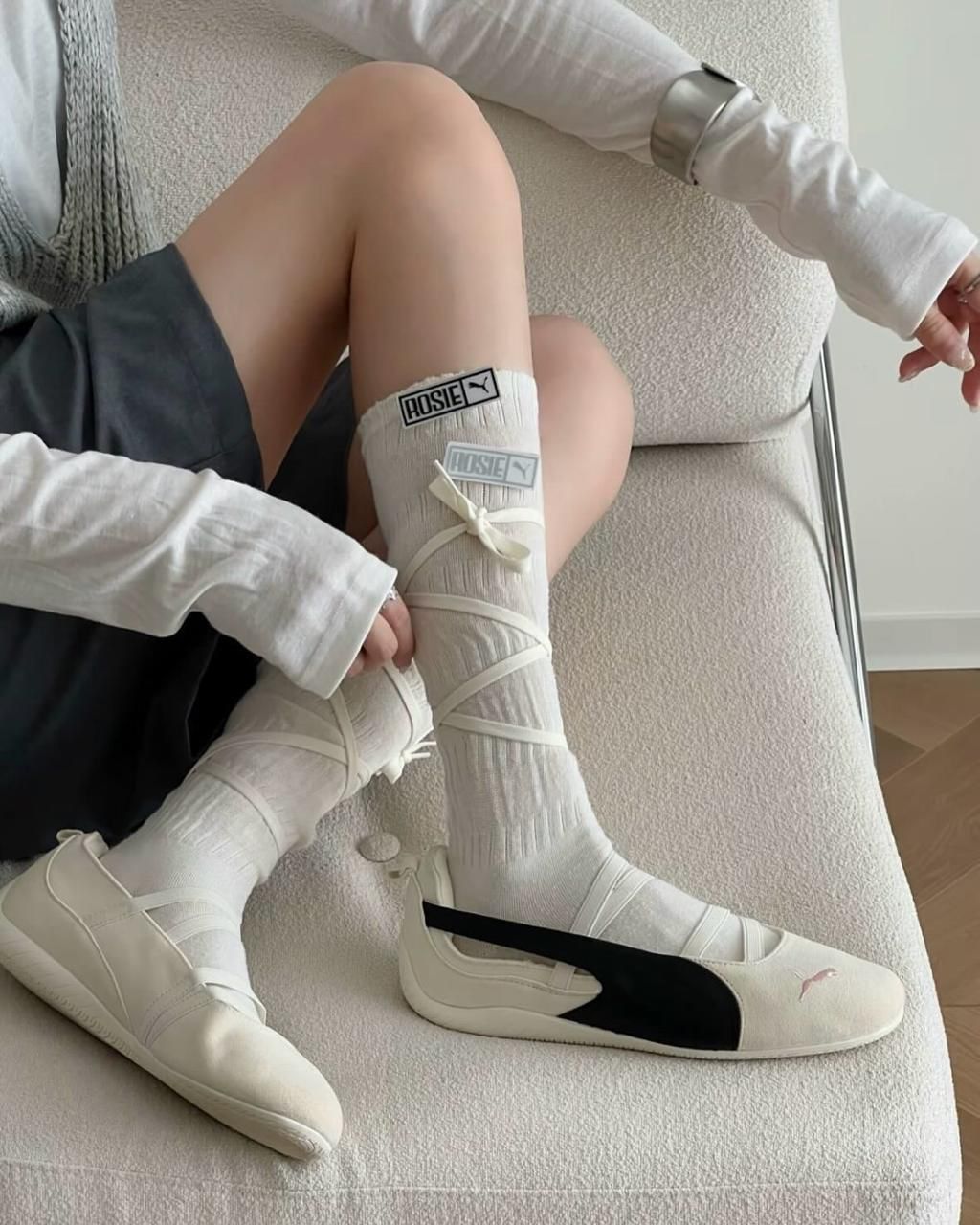 fe8a771c-2ec4-4bbb-8aaf-c3335c1f3732 | UAE SPORT STORE Person sitting on a couch wearing white knee-high socks with a padded wrap and tied ribbons over a white sneakered foot.