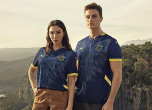fenerbahce_24_25_puma_fourth_kit | UAE SPORT STORE Two models stand outdoors in navy blue and gold soccer jerseys with a canyon backdrop.