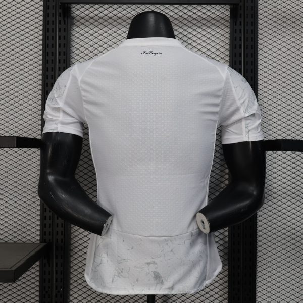Back view of a white lattice-pattern sports jersey on a mannequin, with 'KidSuper' logo at the neck and a metal grid backdrop.