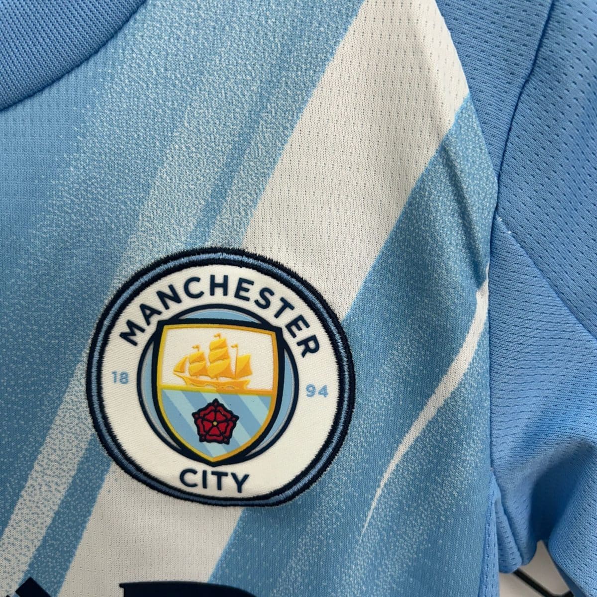 Close-up of a Manchester City crest patch sewn onto light blue denim fabric.