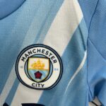 Close-up of a Manchester City crest patch sewn onto light blue denim fabric.