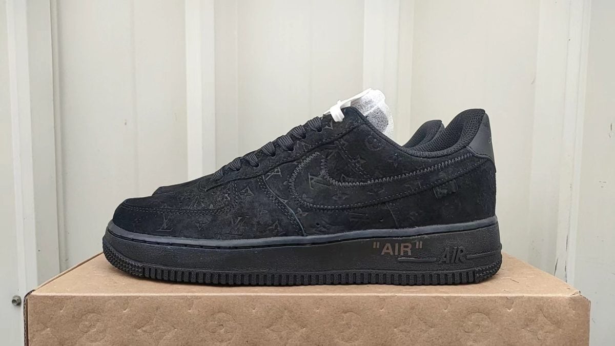 Black suede Nike Air Force 1 sneaker on a brown box, side view with laces and stitched logo pattern visible