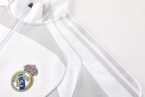 Close-up of a white and light-gray jacket with a Real Madrid crest on the chest and a visible zipper edge.