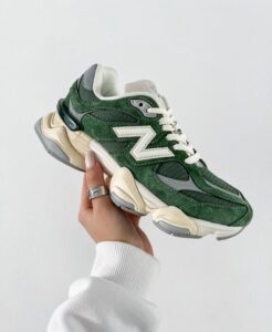 Green suede sneaker with white N logo being held by a hand against a pale background; casual athletic shoe for daily wear.