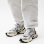 Close-up of feet in gray sweatpants wearing gray-white running shoes with a black Nike swoosh and cream soles.