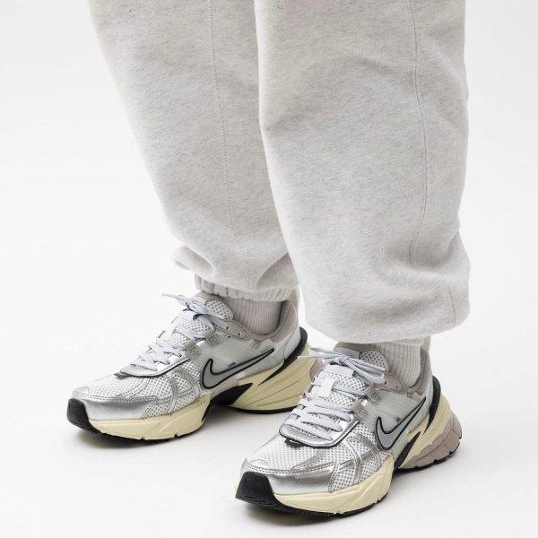 Close-up of feet in gray sweatpants wearing gray-white running shoes with a black Nike swoosh and cream soles.