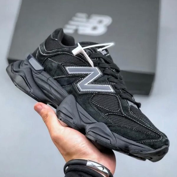 Black chunky New Balance sneaker with a large gray N logo, held in a hand in front of a shoe box.