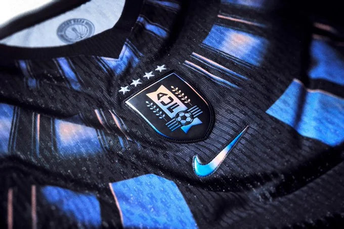 Close-up of a black and blue striped soccer jersey featuring a shield crest with three stars and a blue Nike swoosh.