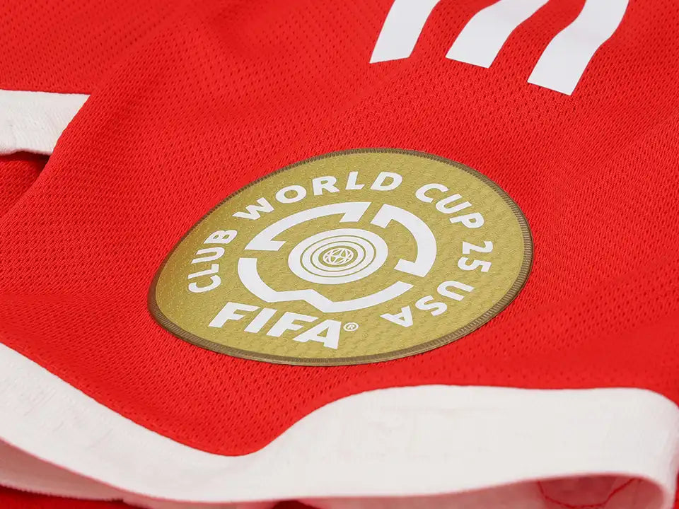 Gold circular patch with FIFA logo on a red sports jersey, surrounded by white trim lines and fabric texture.
