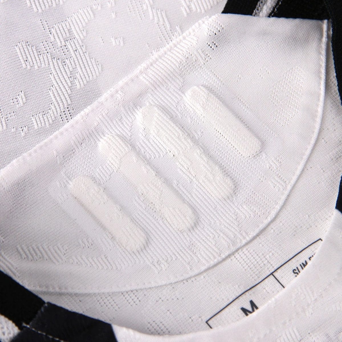 Close-up of a white textured shirt collar with a visible size label, showing intricate jacquard pattern in the fabric.