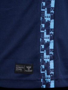 Close-up of navy fabric with a light-blue geometric stripe along a seam and a small black label reading 'AUTHENTIC APPAREL' and 'hummel'.