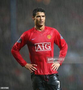 Manchester United footballer in a red jersey standing with hands on hips in the rain.