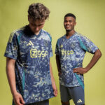 Two young men modeling blue camouflage soccer jerseys with a Ziggo logo, standing against a lime-yellow backdrop.