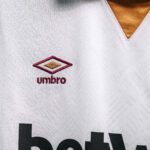 White sports jersey close-up showing the red and gold Umbro diamond logo with 'umbro' text on the chest.
