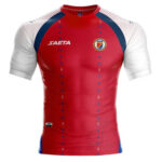 Red athletic rugby-style jersey with white sleeves, blue shoulder panels, a left chest crest, and SAETA branding on the right chest.