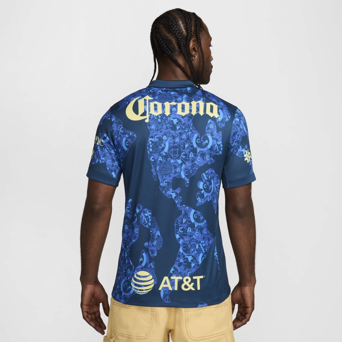 Back view of a man wearing a blue patterned sports jersey with a large yellow 'Corona' logo on the upper back and an AT&T logo near the lower back or hem.