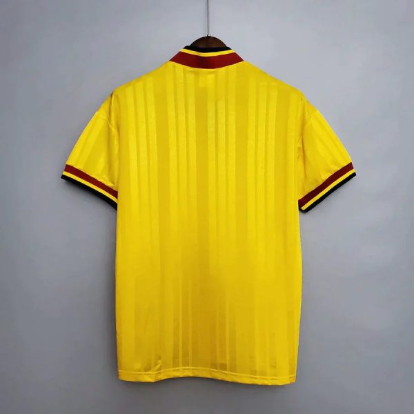 Back view of a bright yellow striped soccer jersey hanging on a hanger, with red and black trim at the collar and sleeve edges.